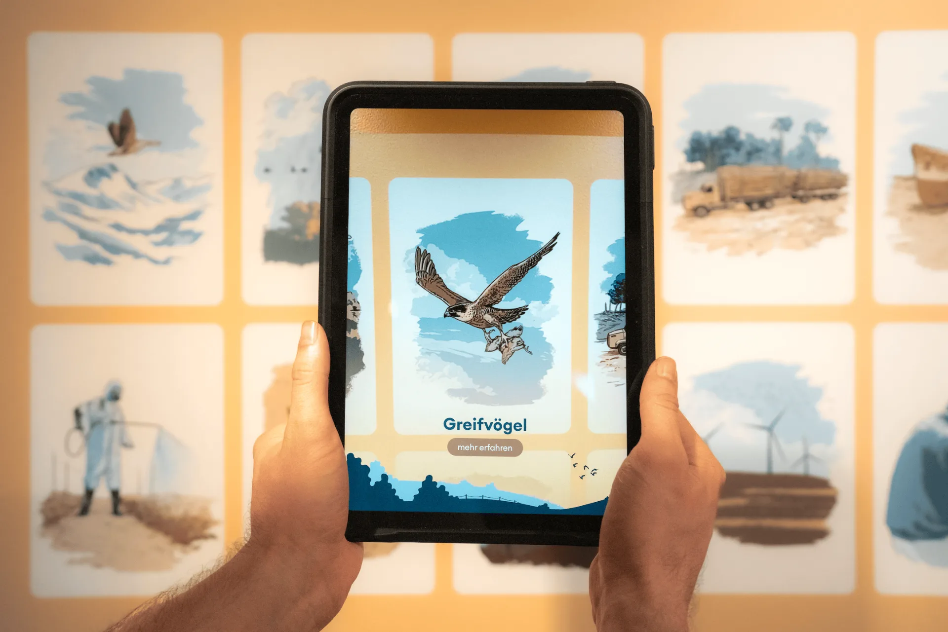 Eine Person hält ein Tablet und richtet die Kamera auf die Ausstellungsstation, um die dort platzierten Illustrationen zu scannen.