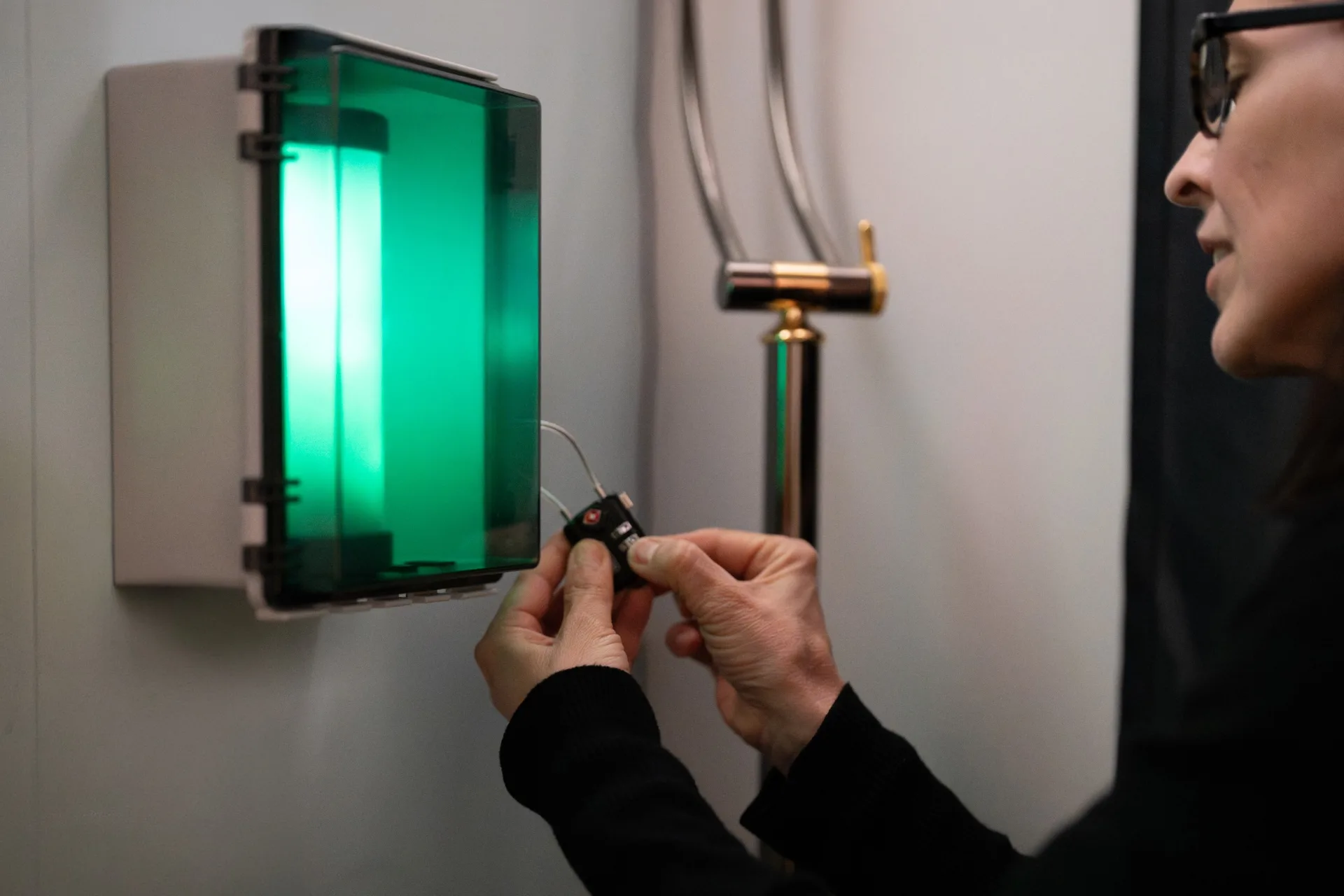 Person öffnet ein Zahlenschloss an einem Wandkasten und holt eine grün leuchtende Plasma-Röhre heraus.