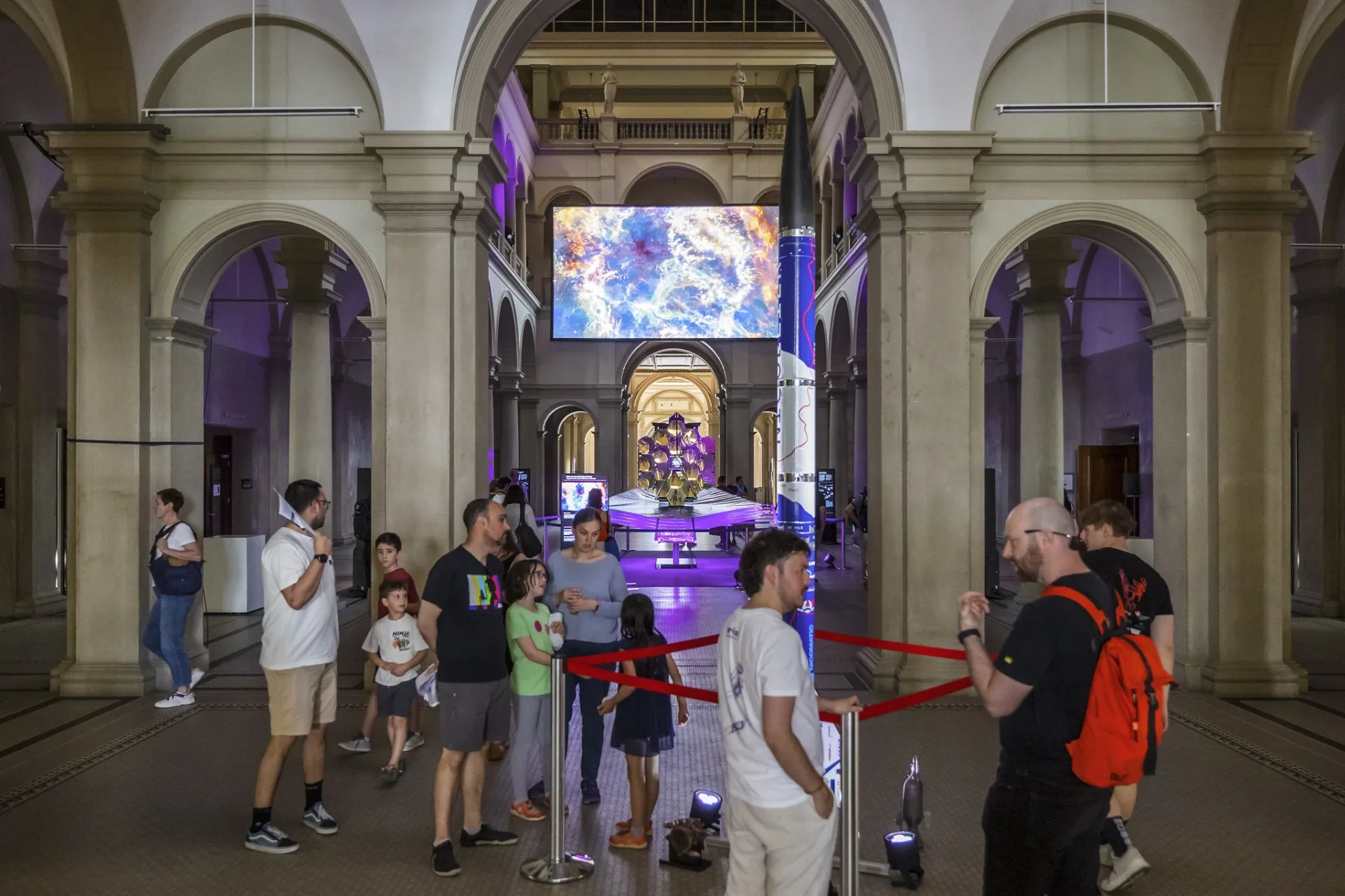 Symmetrischer Blick durch die historischen Rundbögen der ETH Zürich auf die Ausstellung «wow² Space». Im Vordergrund steht ein Raketenmodell, im Hintergrund leuchtet die grosse Medienleinwand.