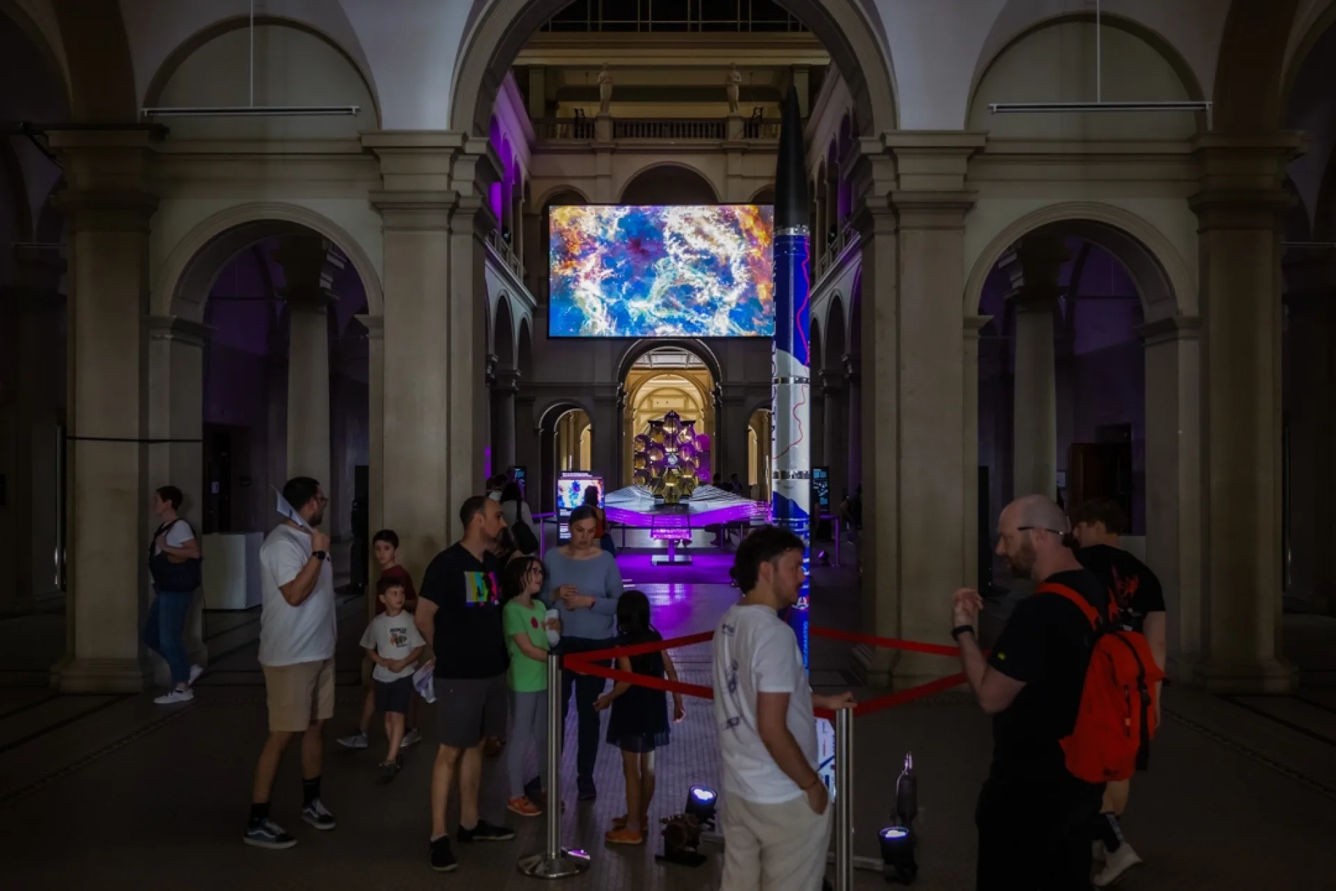 Symmetrischer Blick durch die historischen Rundbögen der ETH Zürich auf die Ausstellung «wow² Space». Im Vordergrund steht ein Raketenmodell, im Hintergrund leuchtet die grosse Medienleinwand.