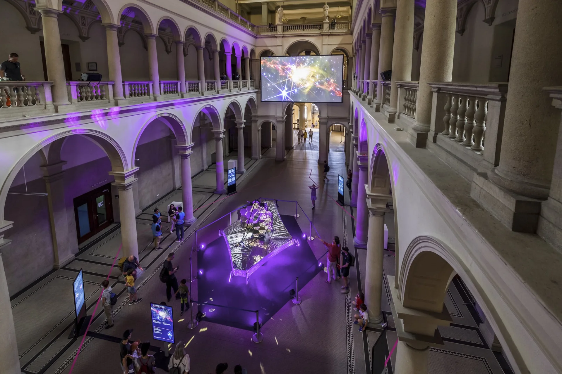 Blick von der Galerie in die temporär abgedunkelte ETH-Haupthalle. Die szenografische Komposition aus dem zentralen Exponat, der grossen Leinwand und der Lichtführung wird als Raumerlebnis sichtbar.