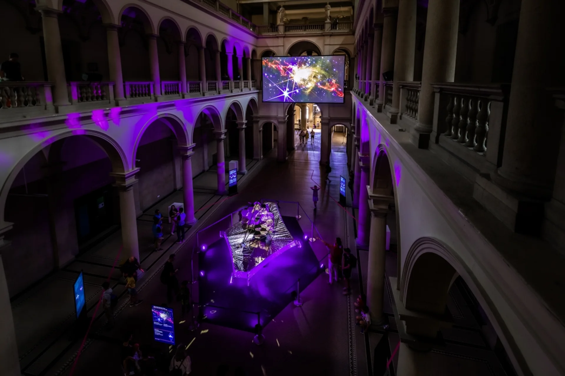 Blick von der Galerie in die temporär abgedunkelte ETH-Haupthalle. Die szenografische Komposition aus dem zentralen Exponat, der grossen Leinwand und der Lichtführung wird als Raumerlebnis sichtbar.