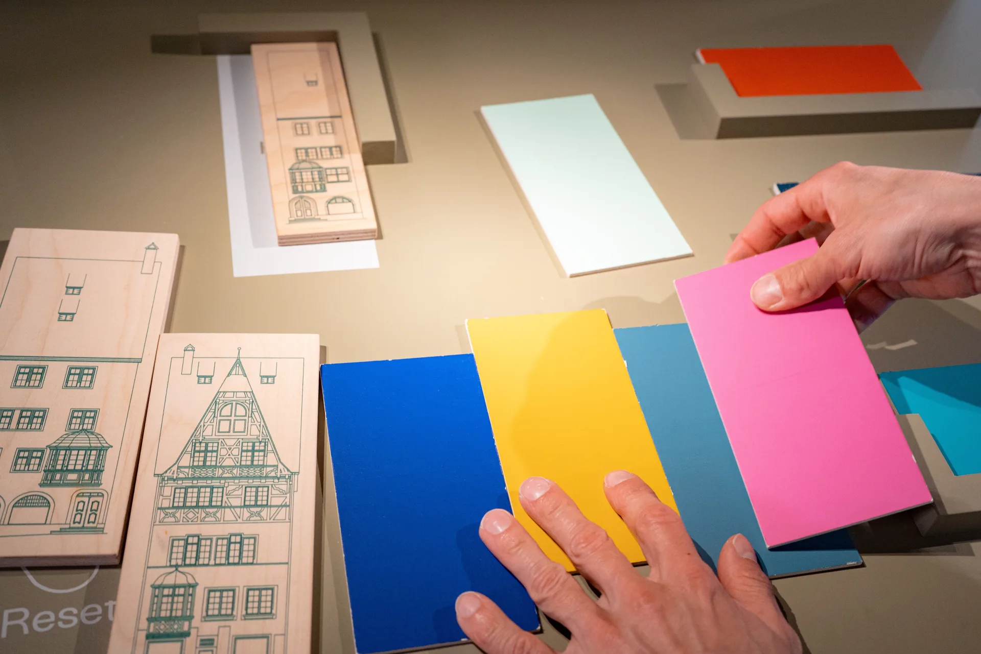 Verschiedene Farbmuster und Häuser-Karten sind auf dem Tisch ausgelegt. Eine Person kombiniert die Farbmuster.