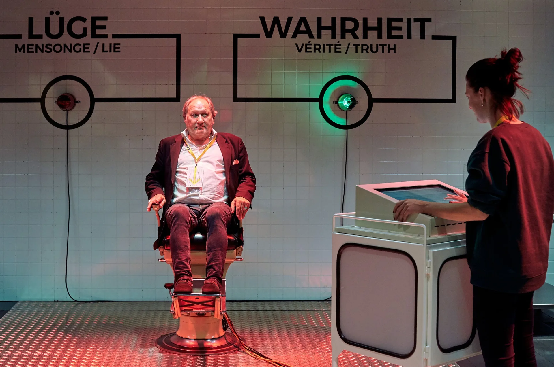 Ein Mann sitzt auf dem Lügendetektor in der Ausstellung und wird von einer jungen Frau befragt.