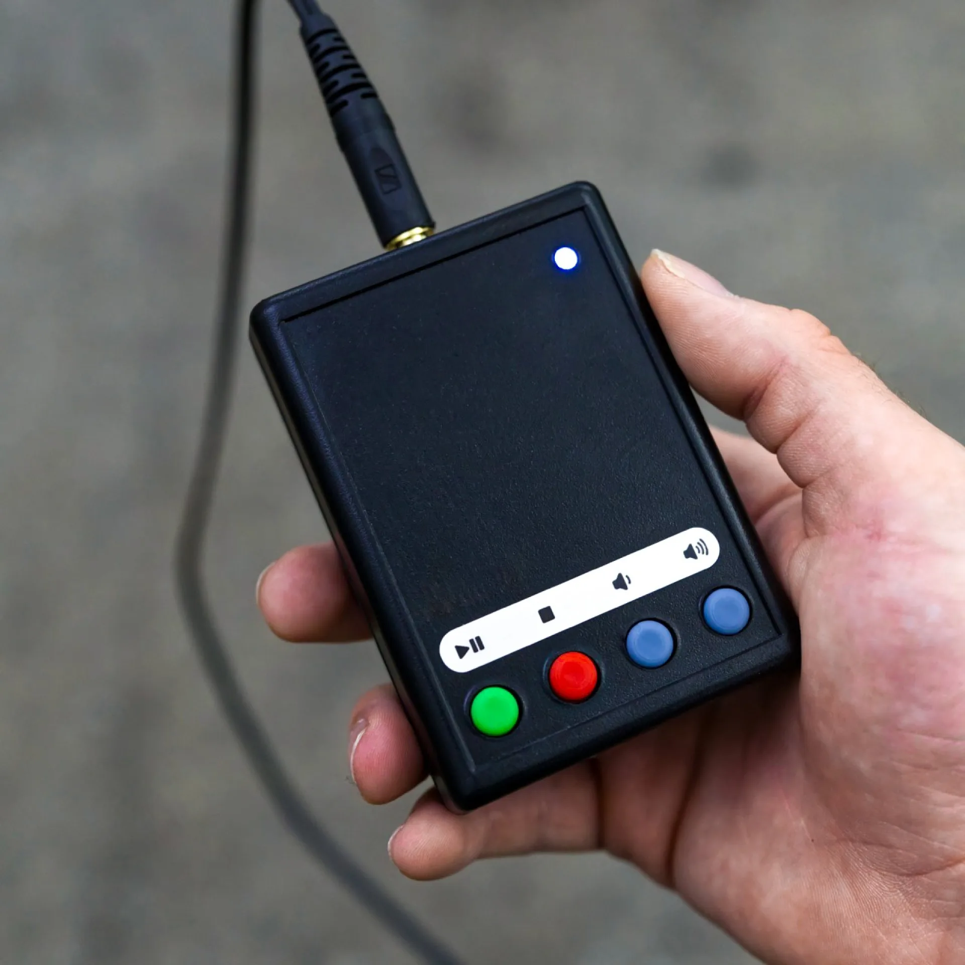 Eine Person hält den Audioplayer in der Hand. Ein Kopfhörer ist am Gerät eingesteckt. Eine LED am Gehäuse leuchtet blau.