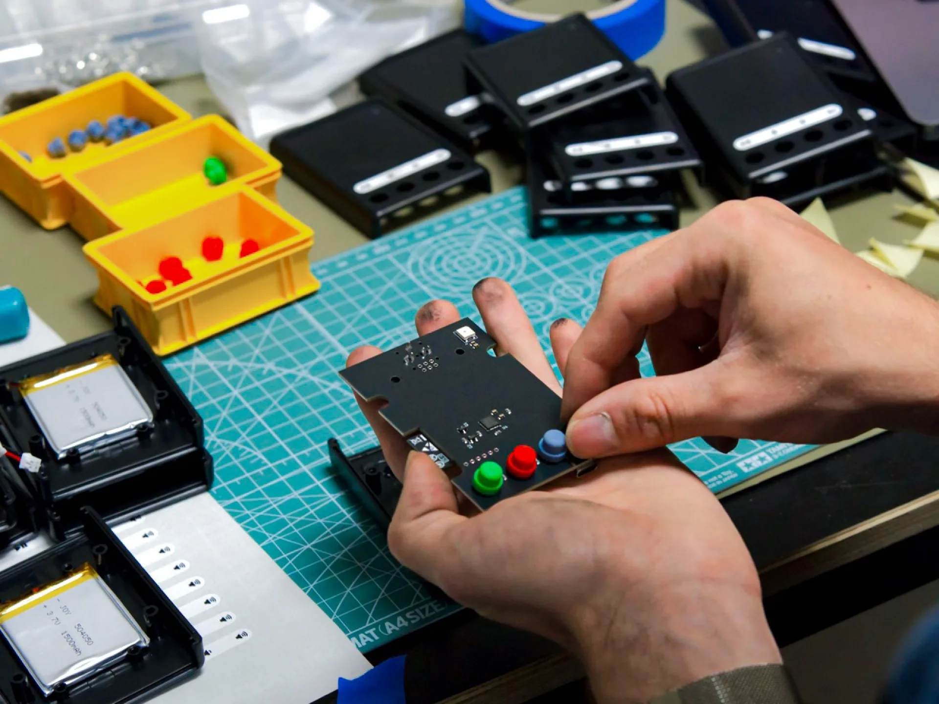 Eine Person montiert die Platine eines Audioplayers. Er liegen Gehäuseteile, Knöpfe und Batterien auf dem Tisch.