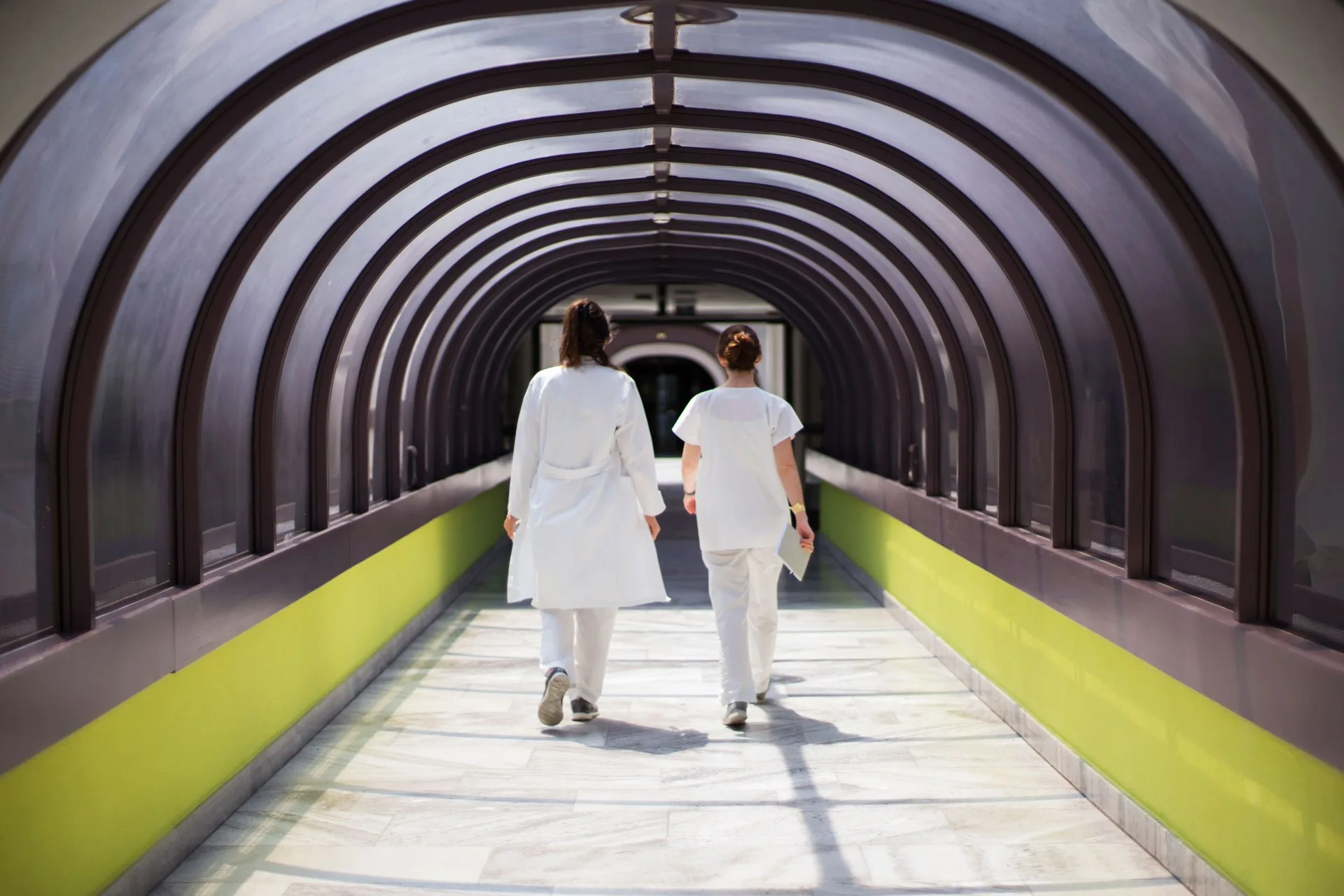 Zwei Ärztinnen laufen durch lichtdurchfluteten Durchgang im Spital.